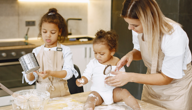 A mom is baking with two little girls, making a big mess.