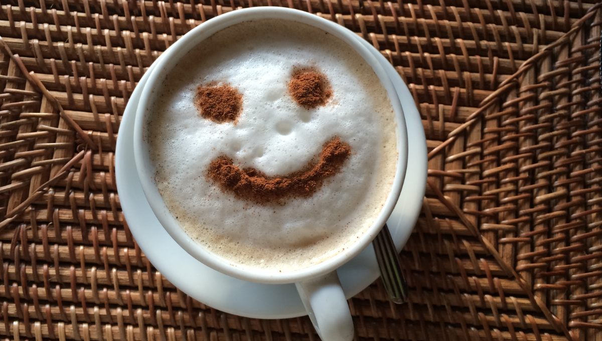 cocoa powder forms a happy face in the foam atop a cup of cappuccino