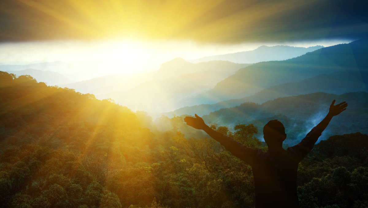 A person raises his arms as the sun rises