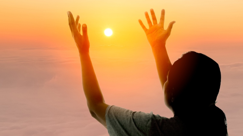 woman lifts up her hands to the setting sun