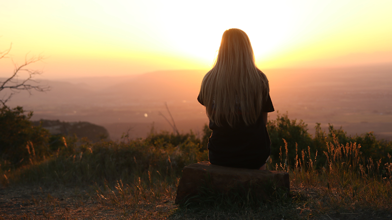 woman sitting alone on a hill at sunset