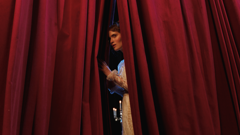 an actress peeks out from behind the stage curtains