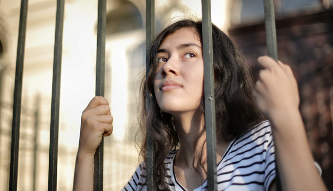 girl looks out from behind bars but appears hopeful